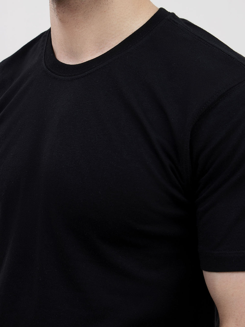 Close-up of men's black round neck t-shirt, fabric texture and neckline detail, white background