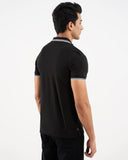 Close-up black polo, white tipped collar, crest logo on chest