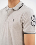 Close-up light grey polo, black tipped collar, crest logo on chest, "8" on sleeve