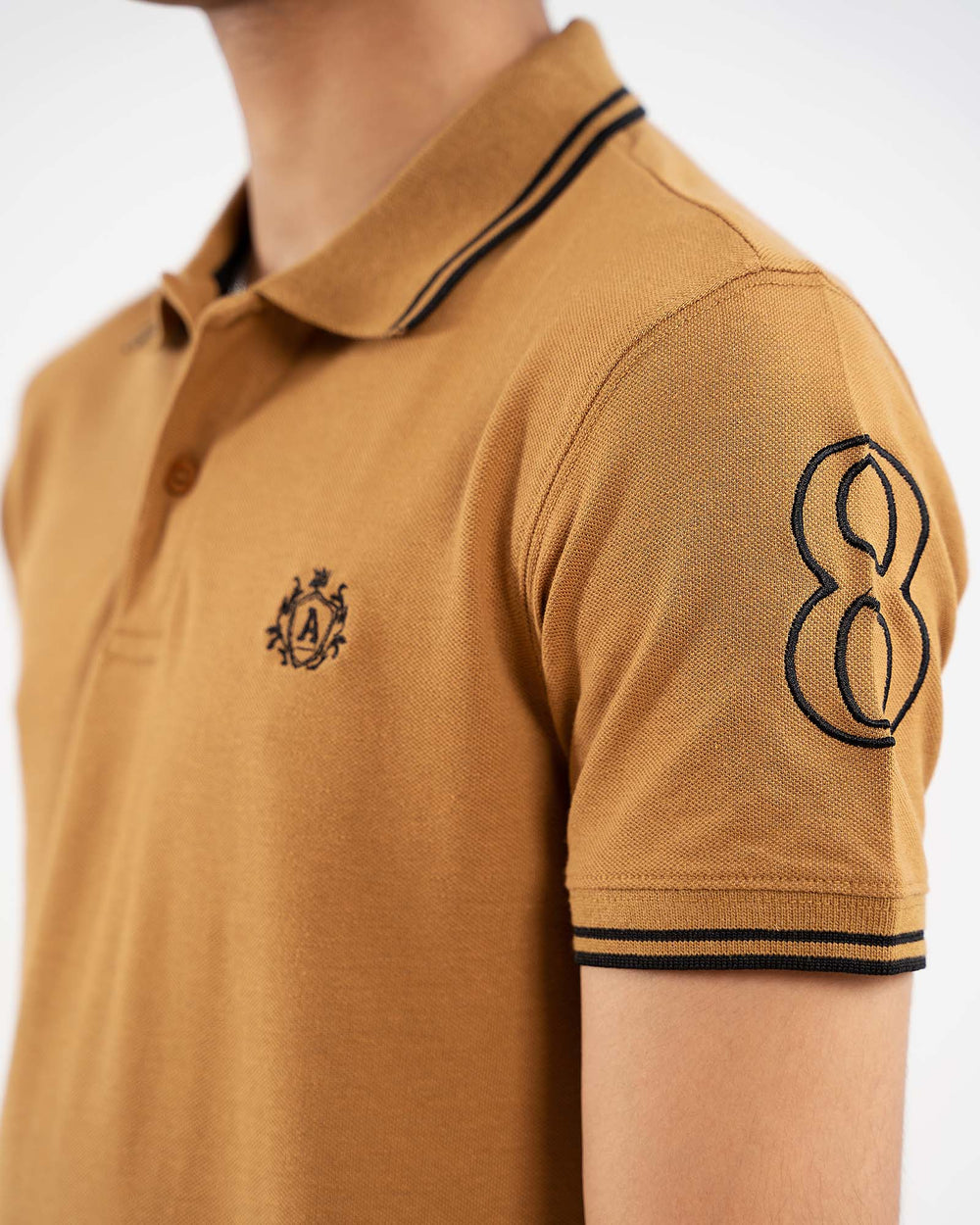 Close-up camel tan polo, black tipped collar, crest logo on chest, "8" on sleeve