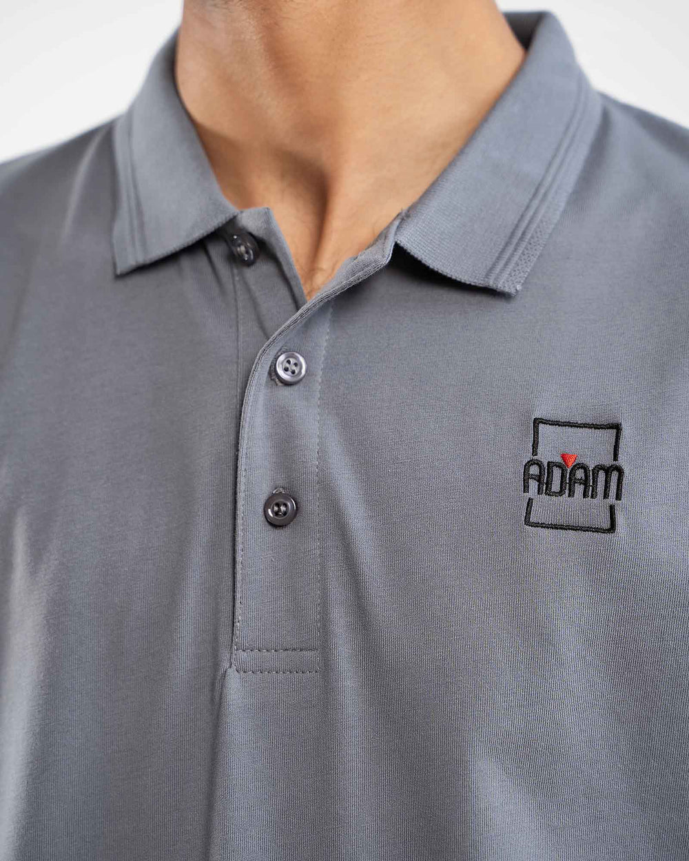Close-up of grey polo shirt with small embroidered "Adam" square box logo patch on chest