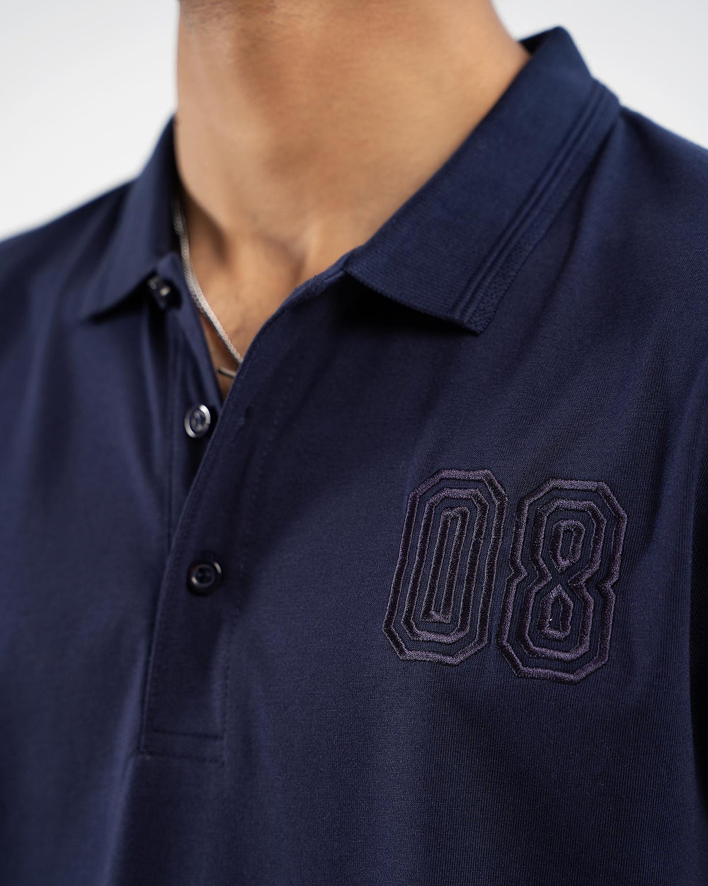 Close-up of navy blue polo shirt with tonal embroidered outlined "08" number on chest